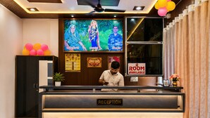 A reception desk with a 'ROOM AVAILABLE' sign, a television displaying a religious figure, and a ceiling fan. - Hotel Luxury Palace Vrindavan (Vrindavan)