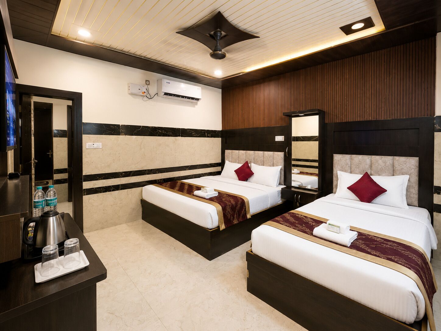 A hotel room with two beds, a minibar, a mirror, and an air conditioning unit.
