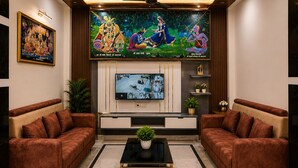 A living room with two sofas, a coffee table, a TV, and a mural on the wall. - Hotel Luxury Palace Vrindavan (Vrindavan)