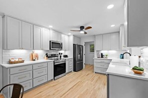 A modern kitchen with grey cabinets, stainless steel appliances, and a wooden floor.