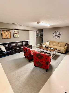 A living room with a brown leather couch, a beige sofa, and two red floral armchairs. There is a white coffee table in the center. - Cozy Guest Suite near Downtown Lee's Summit (Lee's Summit)