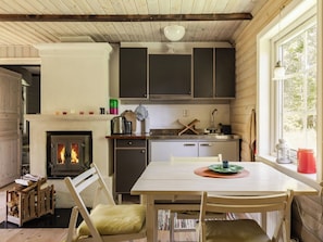 A cozy cabin interior with a fireplace, wooden dining table, and a kitchen area.