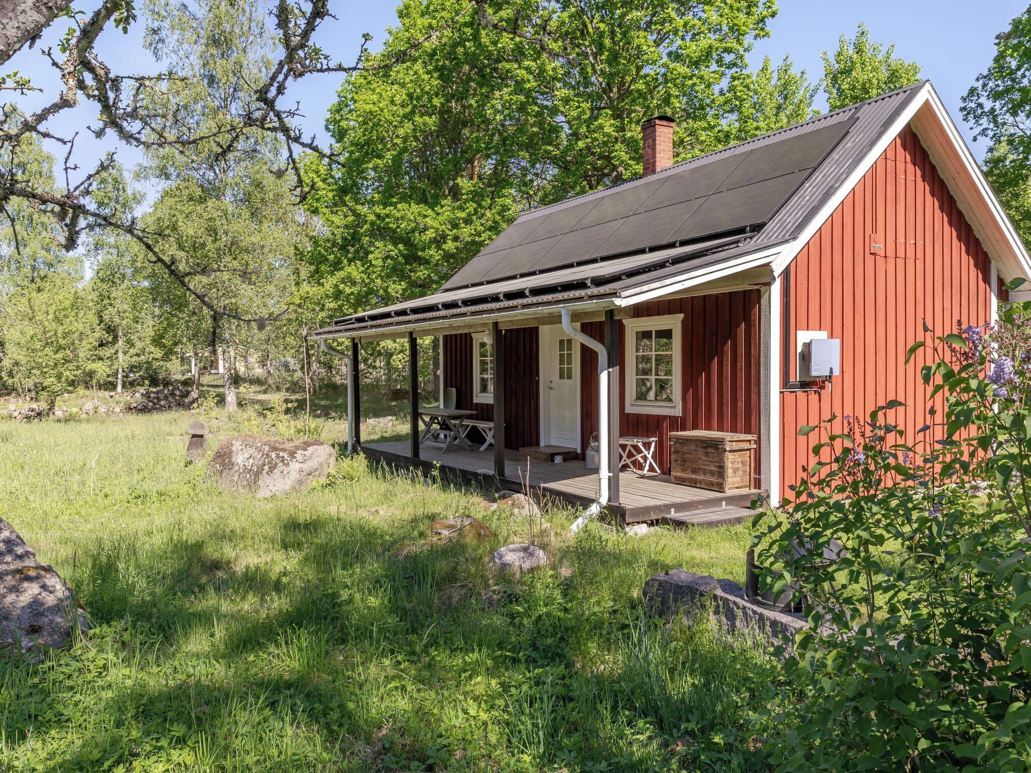 A red wooden cabin with a porch, surrounded by greenery and trees.