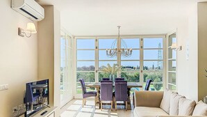 A spacious living room with a large window, a chandelier, a sofa, and a dining area.