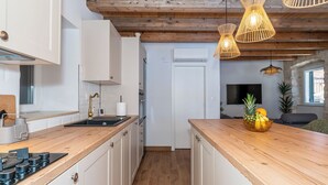 A modern kitchen with wooden countertops, white cabinets, a built-in stove, and a dining area with a fruit bowl. - Vacation home Nina by Interhome (Brač/Donji Humac)