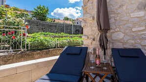 A terrace with two lounge chairs, a table with a bottle and glasses, and a stone wall. - Vacation home Nina by Interhome (Brač/Donji Humac)