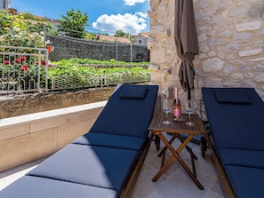 Una terrazza con due poltrone, un tavolo con una bottiglia e dei bicchieri, e un muro in pietra.