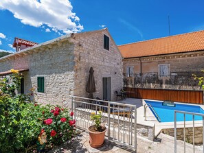 A stone building with a tiled roof, a swimming pool, and a garden with roses.