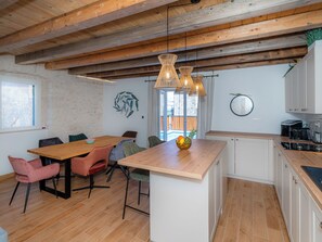 Une cuisine moderne avec des poutres en bois, un coin repas avec des chaises colorées et une grande fenêtre.
