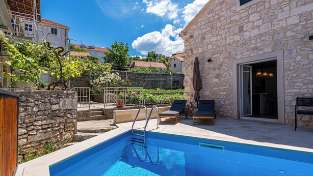 A swimming pool with a stone wall, a wooden fence, and a stone building in the background. - Vacation home Nina by Interhome (Brač/Donji Humac)