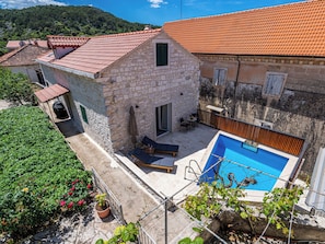 Una casa in pietra con tetto in tegole rosse, una piscina e un patio con mobili da esterno.