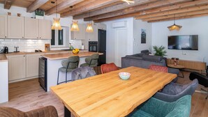 A modern kitchen with wooden beams, a dining area with a wooden table, and a living space with a sofa and TV. - Vacation home Nina by Interhome (Brač/Donji Humac)