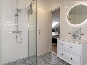 Un bagno moderno con cabina doccia in vetro, un mobile lavabo bianco con cassetti e uno specchio rotondo con un cartello sopra.