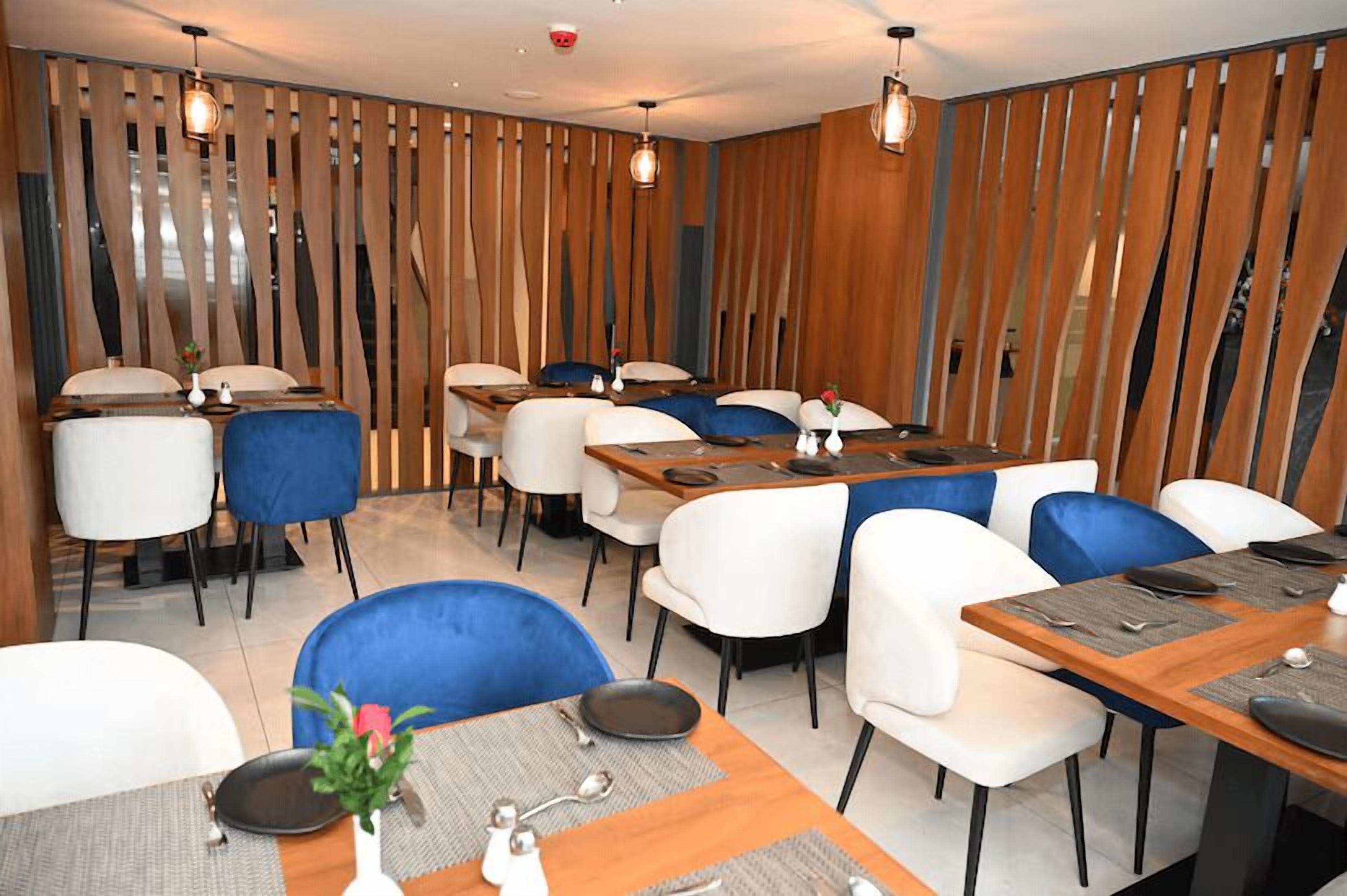 A restaurant with a modern interior, featuring wooden slats on the walls, white and blue chairs, and wooden tables.