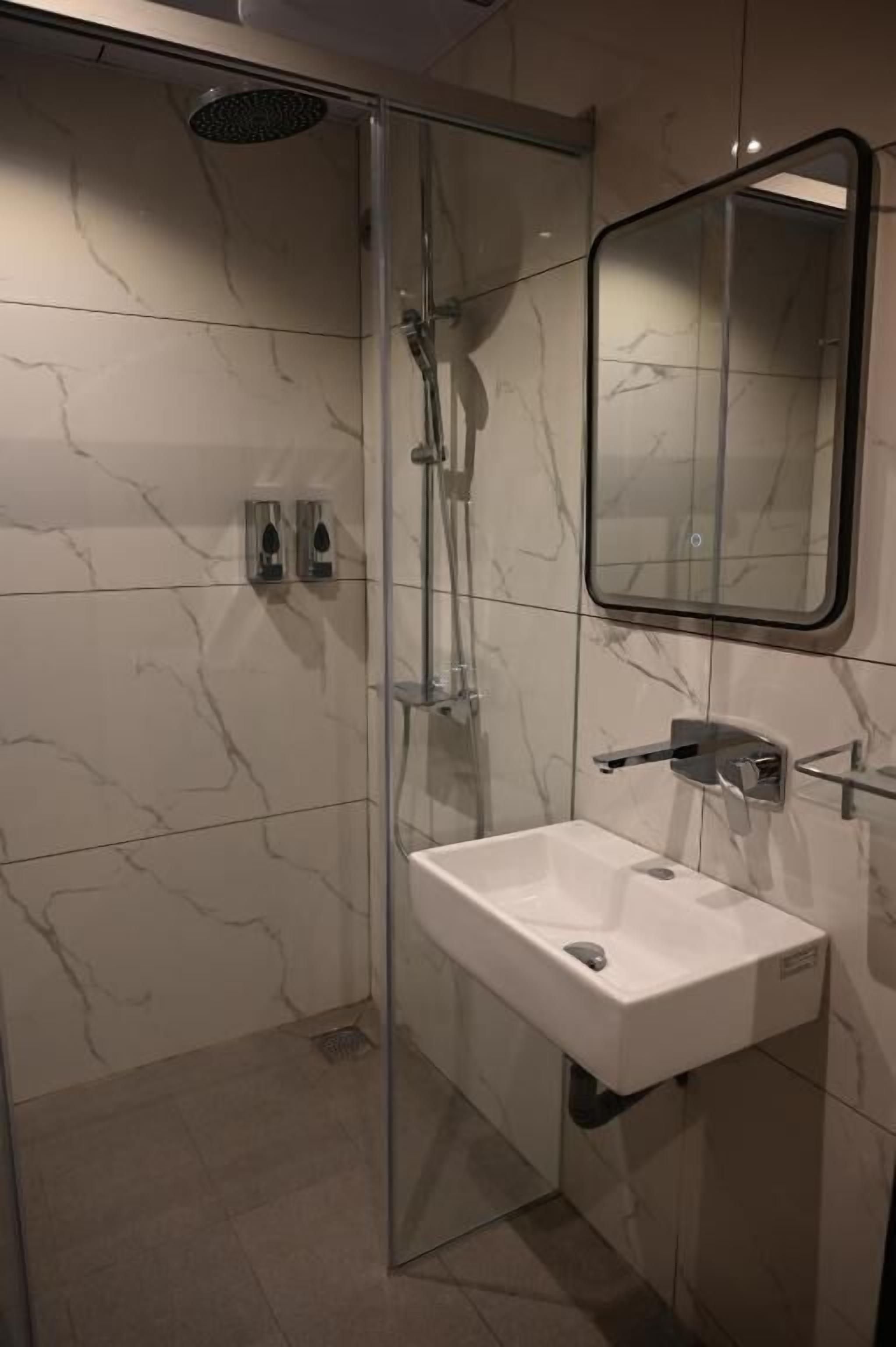 A modern bathroom with a glass-enclosed shower, a white sink, and a mirror.