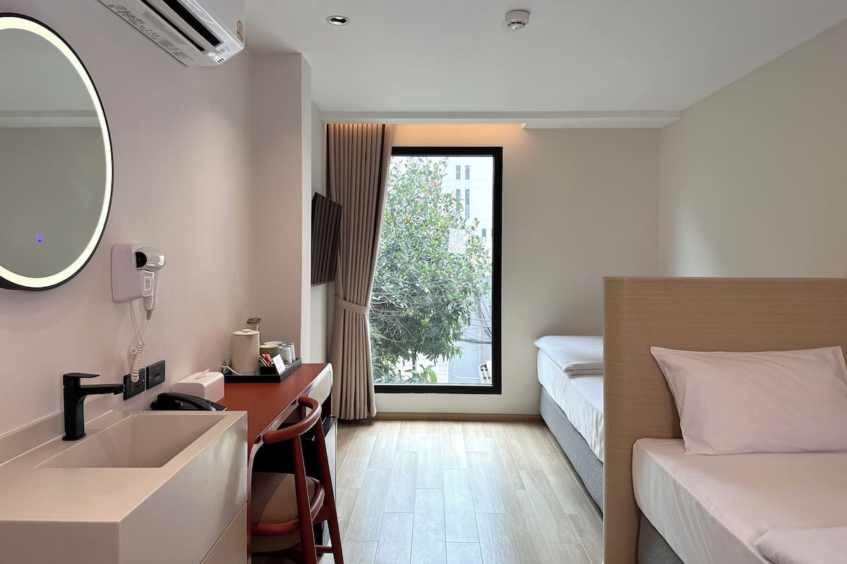 A hotel room with a bed, a desk with a chair, a large mirror, a sink, and a window with curtains.