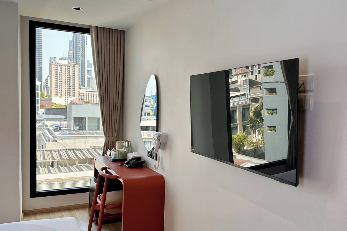 A hotel room with a large window, a desk with a telephone, a chair, and a bed.