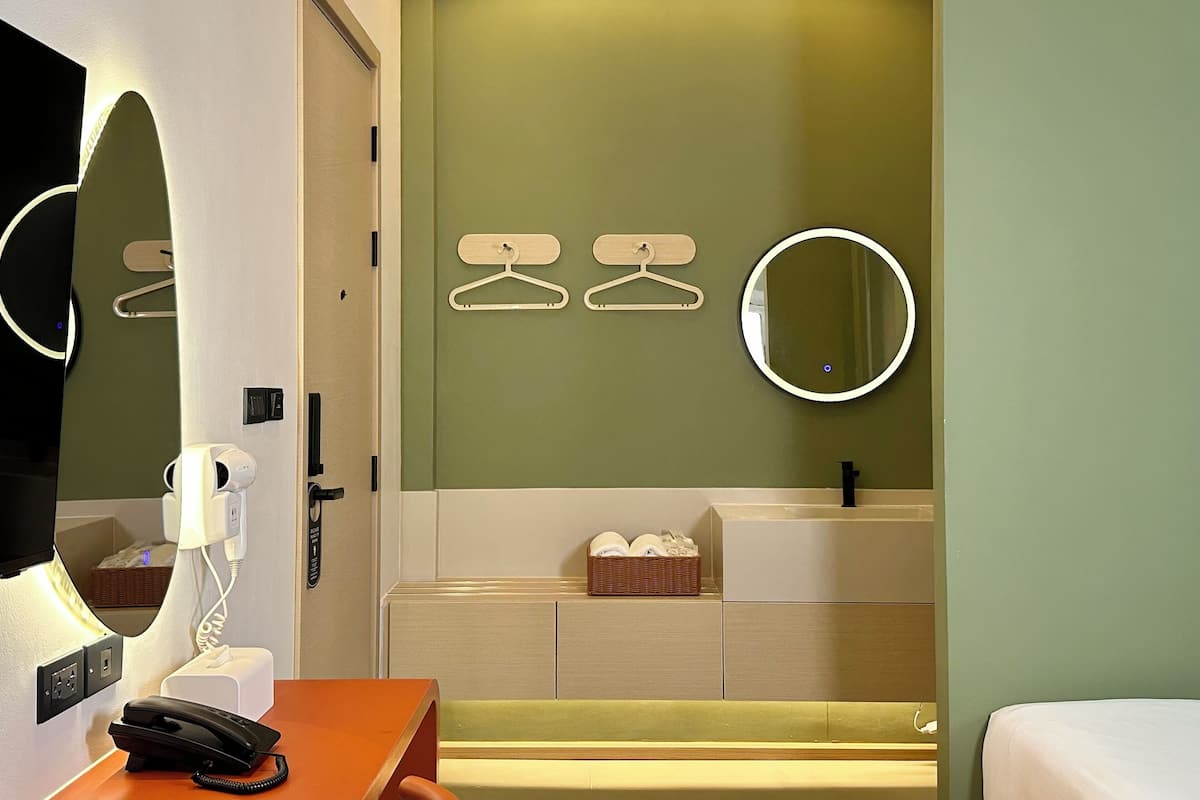 A hotel room with a bed, a desk with a telephone, a mirror, and a wall-mounted light.