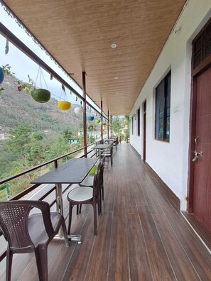 A covered outdoor seating area with tables and chairs, a wooden ceiling, and a view of a mountainous landscape. - Kedar Chaukhamba Homestay (Jakholi)