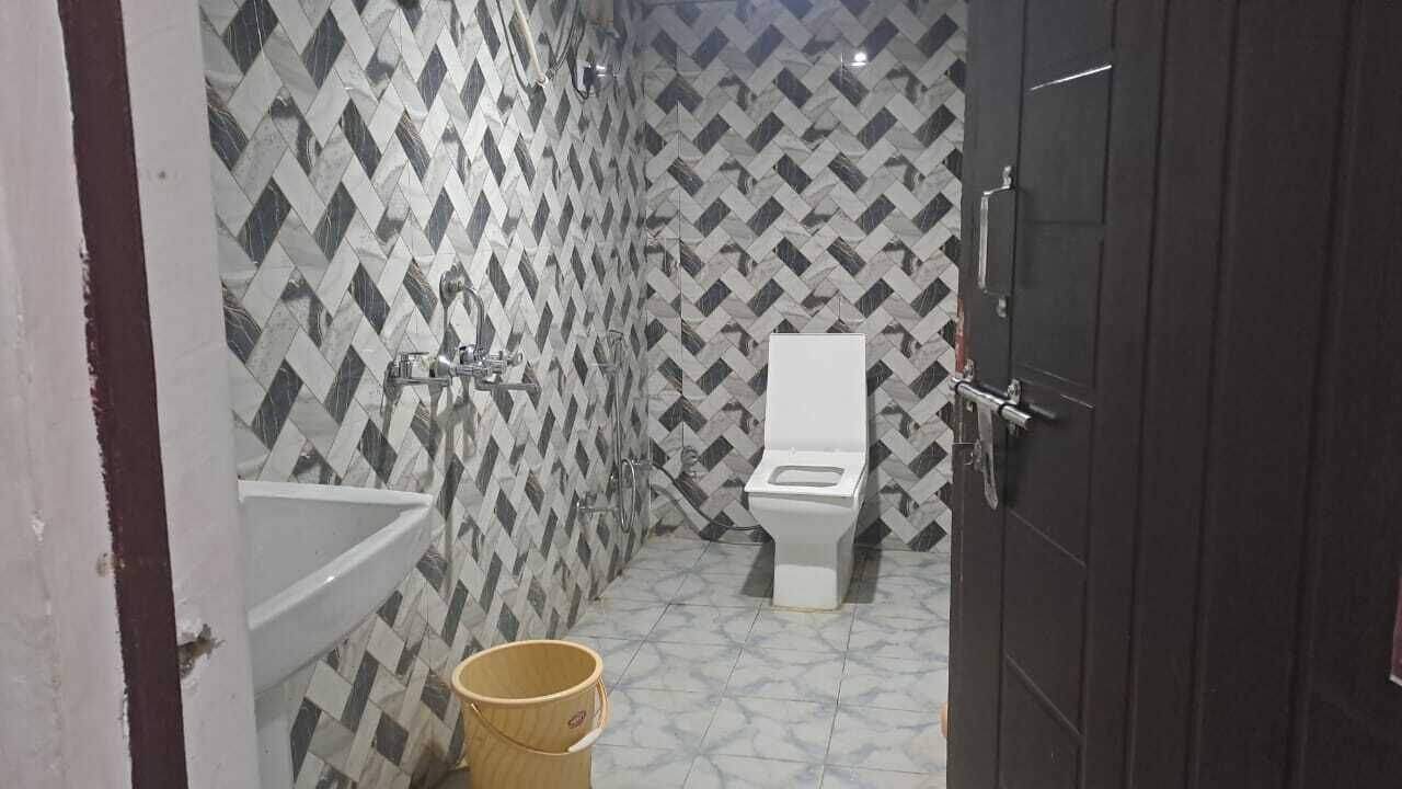 Un baño con pared de baldosas estampadas, inodoro blanco, lavamanos y un cubo de madera.