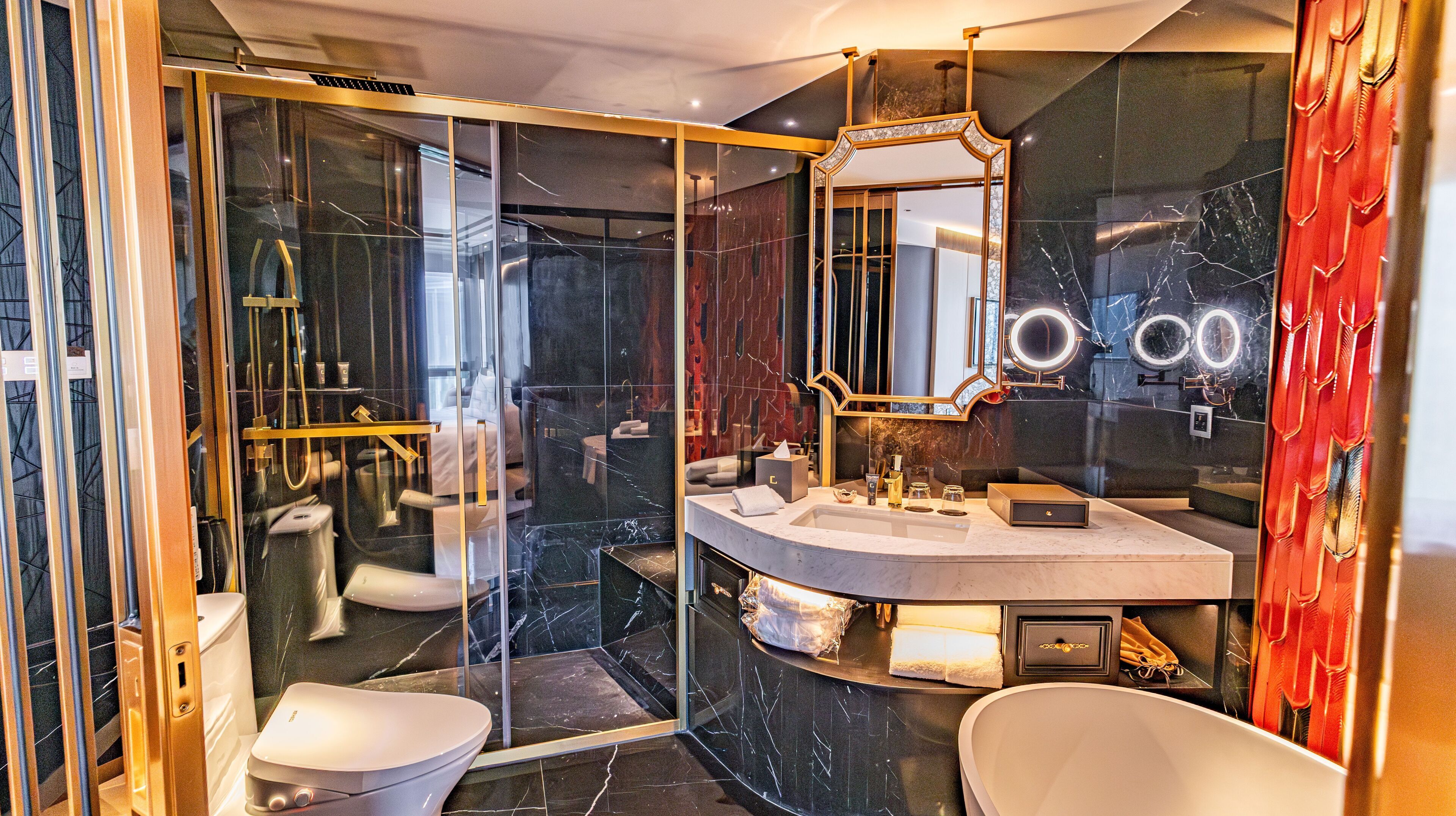 Un baño moderno con ducha de vidrio, tocador de mármol y un espejo grande con marco dorado.