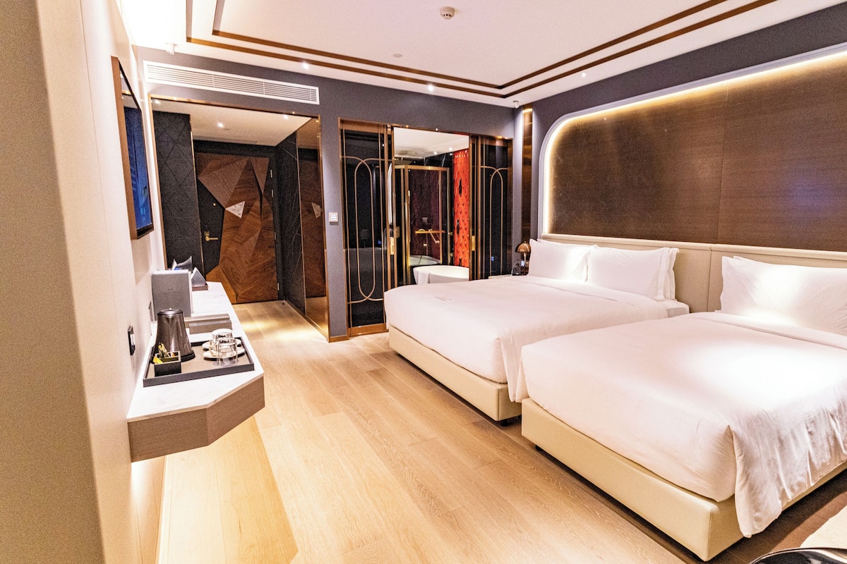A modern hotel room with two beds, a small desk, and a mirror.