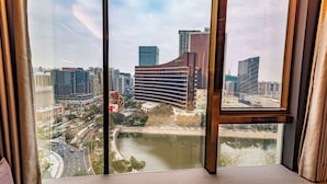 Vista de um andar alto, com um horizonte urbano que inclui edifícios modernos, um rio e uma área de parque.