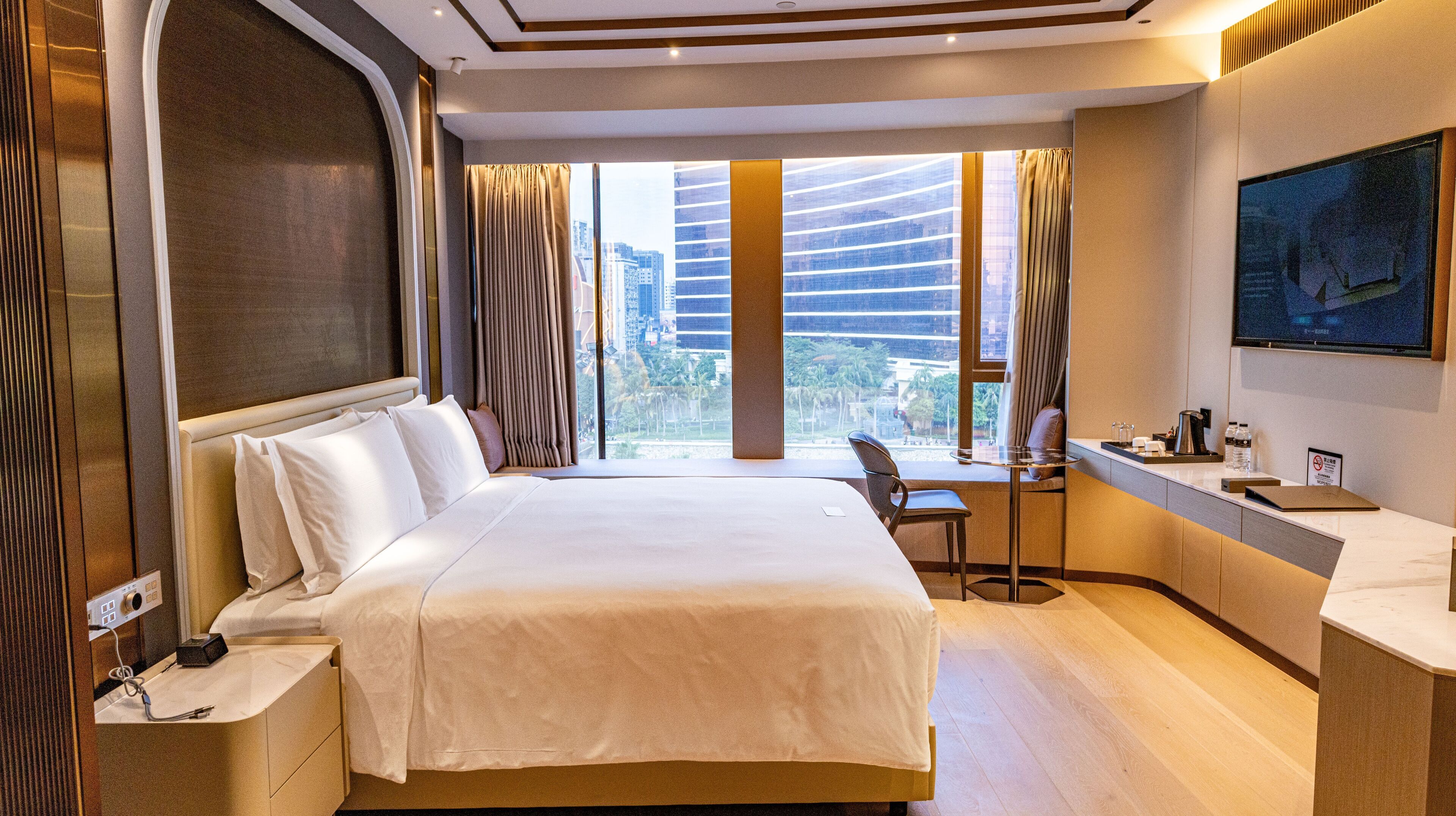 Habitación de hotel con una cama grande, un escritorio con una silla, un televisor y vistas a la ciudad.