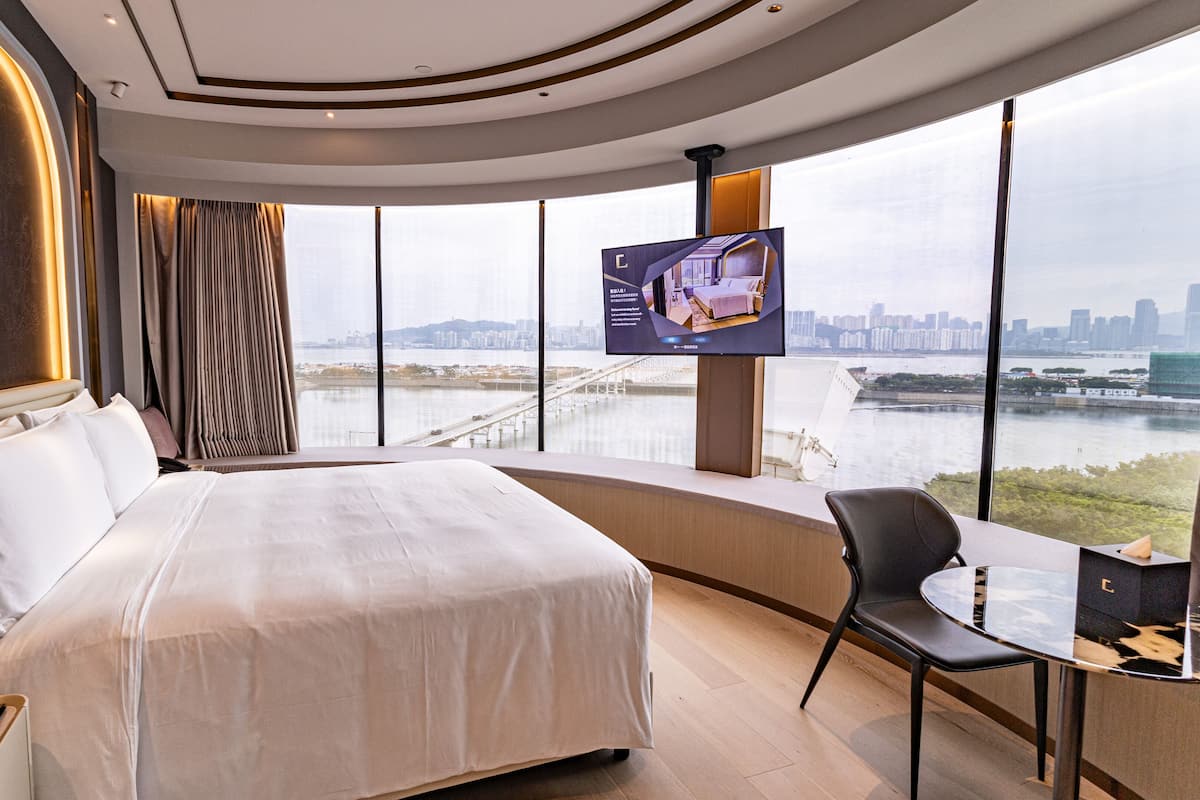 A modern hotel room with a large bed, a desk, and a TV displaying a cityscape.