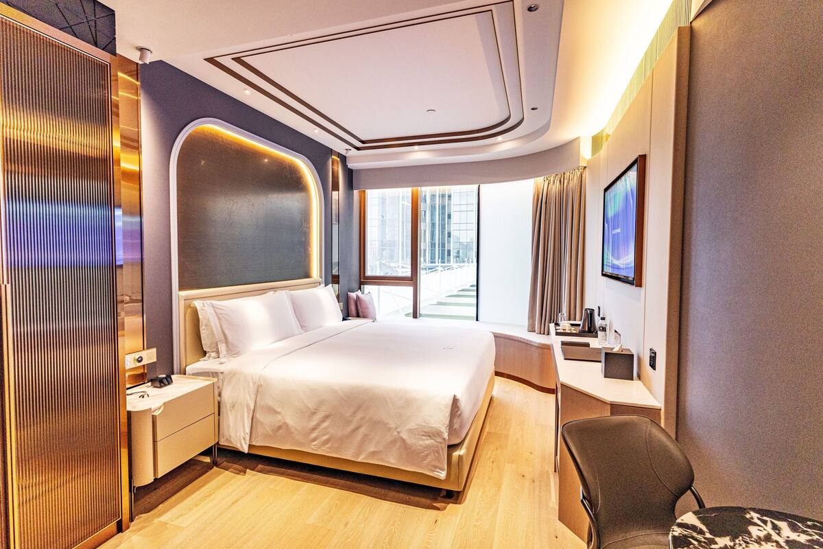 A modern hotel room with a large bed, bedside tables, a desk, and a TV.