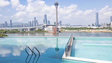 A swimming pool with clear blue water, a tall tower in the background, and a city skyline.
