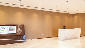 Uma área de recepção com um painel digital, um balcão de atendimento e uma parede de madeira.