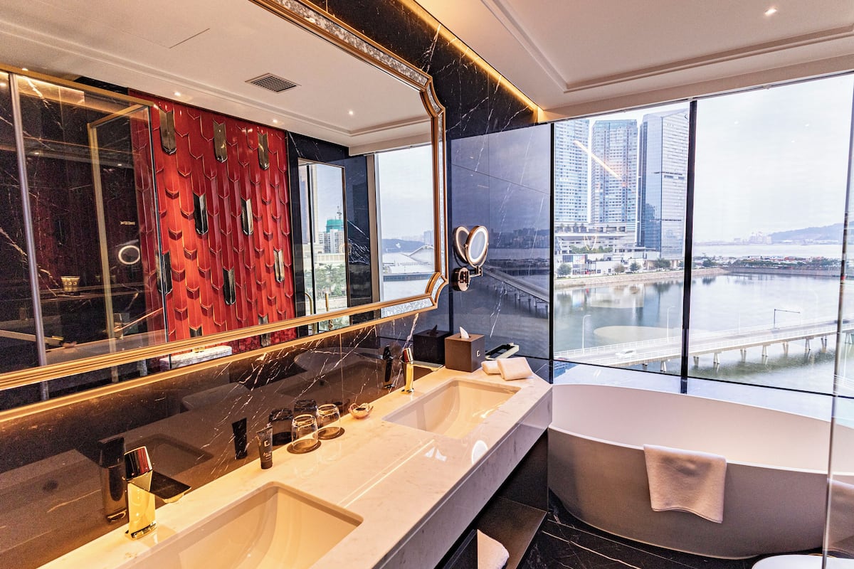 A modern bathroom with a large mirror, dual sinks, and a freestanding bathtub.