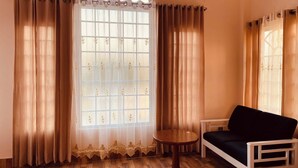 A room with a large arched window, beige curtains, a round wooden table, and a black sofa. - Hotel Sea Inn Saint Martin (Saint Martin's Island)