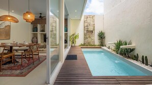 Un espace piscine moderne avec une terrasse en bois, des portes vitrées et un mur en pierre.