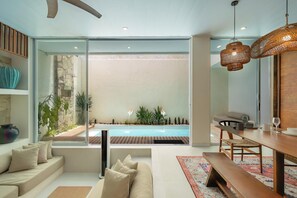 A modern living room with a glass wall, a pool, and a dining area. - Sandwave Villa by Betterplace (Ungasan)