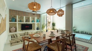 Un salon moderne comprenant un coin repas, un ventilateur de plafond et un téléviseur fixé au mur.