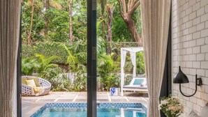 A bedroom with a large bed, a view of a swimming pool, and a white brick wall. - TBK VILLA VAGATOR 15 (Vagator)