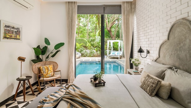 A bedroom with a large bed, a view of a swimming pool, and a chair with a plant. - TBK VILLA VAGATOR 15 (Vagator)
