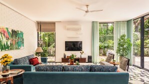 A living room with a sofa, TV, and a view of greenery. - TBK VILLA VAGATOR 15 (Vagator)