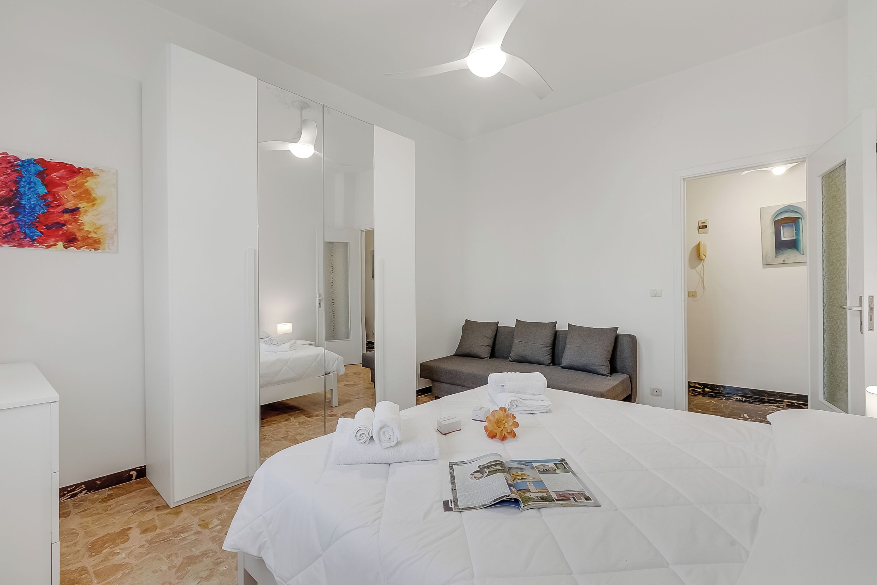 A hotel room with a bed, a sofa, a mirror, and a painting on the wall.