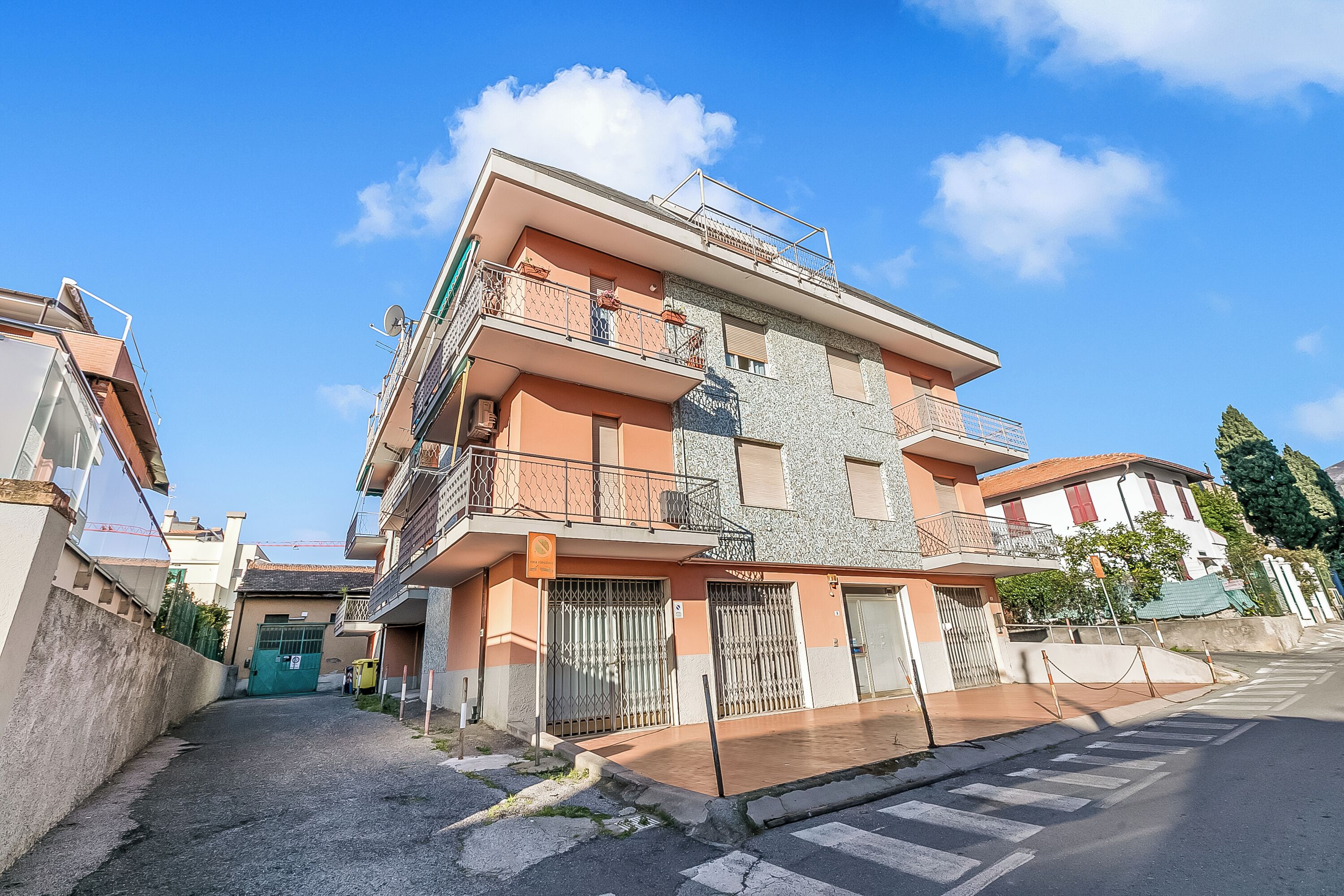 A multi-story residential building with balconies, a gated entrance, and a clear sky.