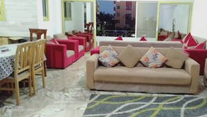 Una sala de estar con un sofá color beige, sillones rojos y un comedor con mesa y sillas.