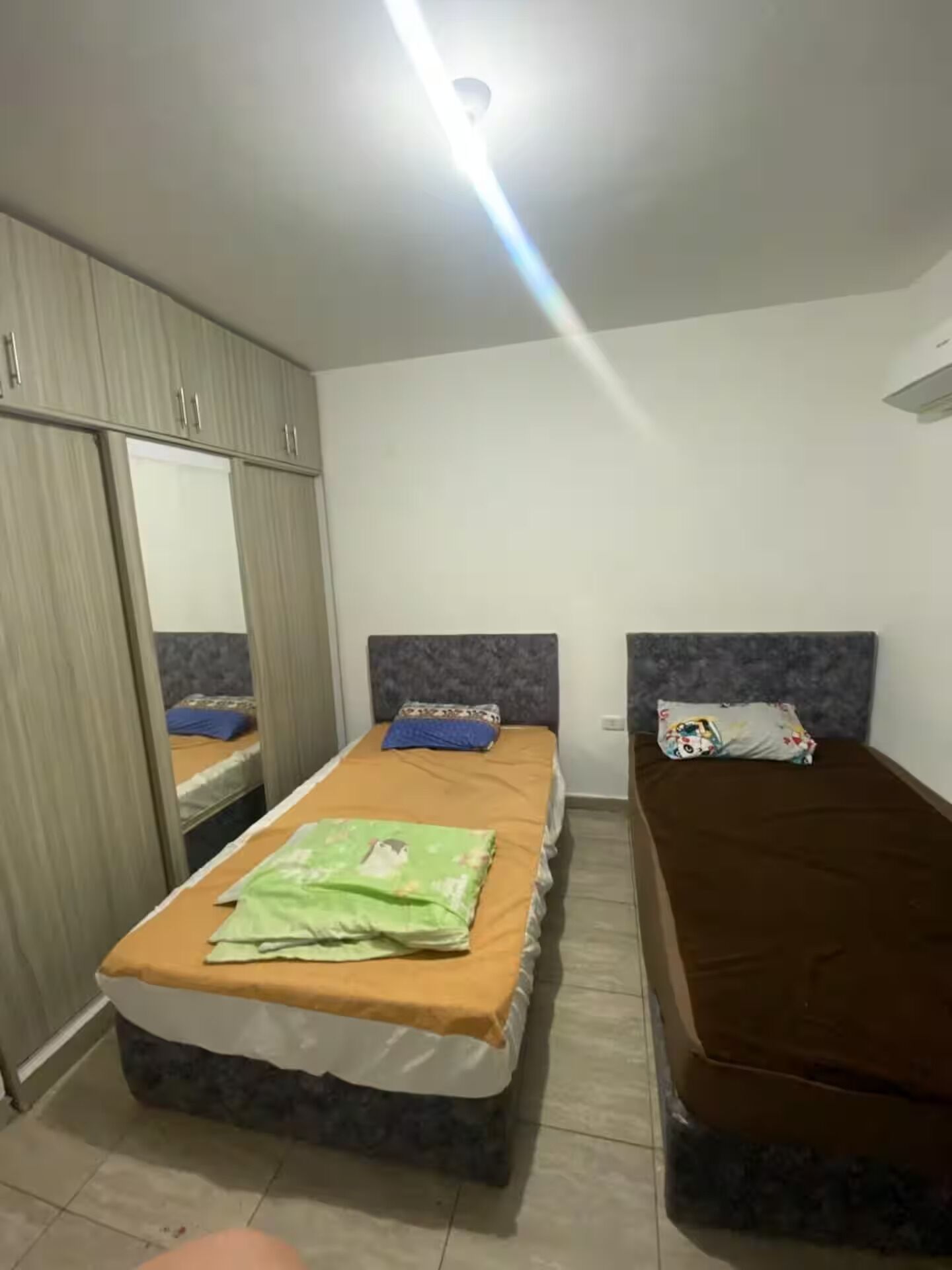 Een slaapkamer met twee bedden, een kledingkast en een plafondlamp.