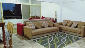 Una sala de estar con dos sofás color crema, un sillón rojo, un tapete estampado y un televisor sobre una mesa.