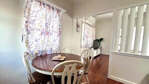 A dining area with a round table, white chairs, floral curtains, and a white console table with a television. - Cosy spacious Holiday Family Home within minutes walking distance to waterfront (Margate)