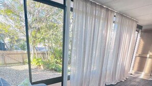 A room with a large window, a sofa with patterned cushions, a bench, and a view of greenery outside. - Cosy spacious Holiday Family Home within minutes walking distance to waterfront (Margate)