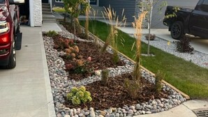 A residential driveway with a landscaped garden bed, a parked SUV, and a house with a stone facade and a garage. - Starling Heaven (Fort Saskatchewan)