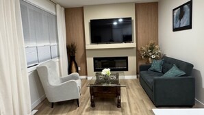 A living room with a sofa, armchair, TV, fireplace, and a coffee table. - Starling Heaven (Fort Saskatchewan)
