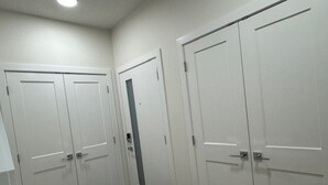 A hallway with three white doors, a black doormat, and a light ceiling. - Starling Heaven (Fort Saskatchewan)